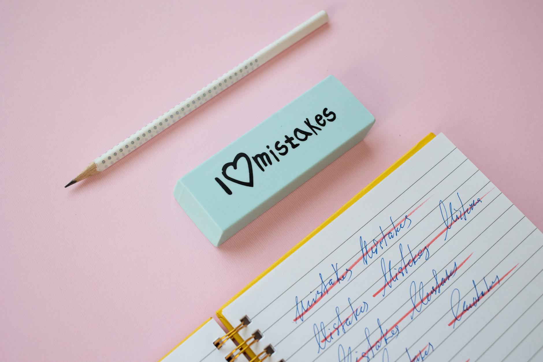 A blue eraser with 'I Love Mistakes' next to a pencil and crossed-out text on a pink background.