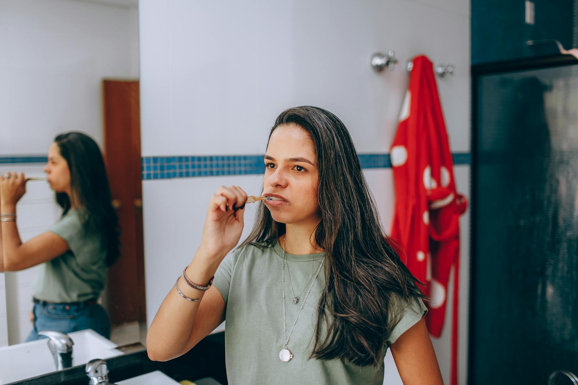 Young woman brushing teeth in a modern bathroom with a red towel hanging nearby.