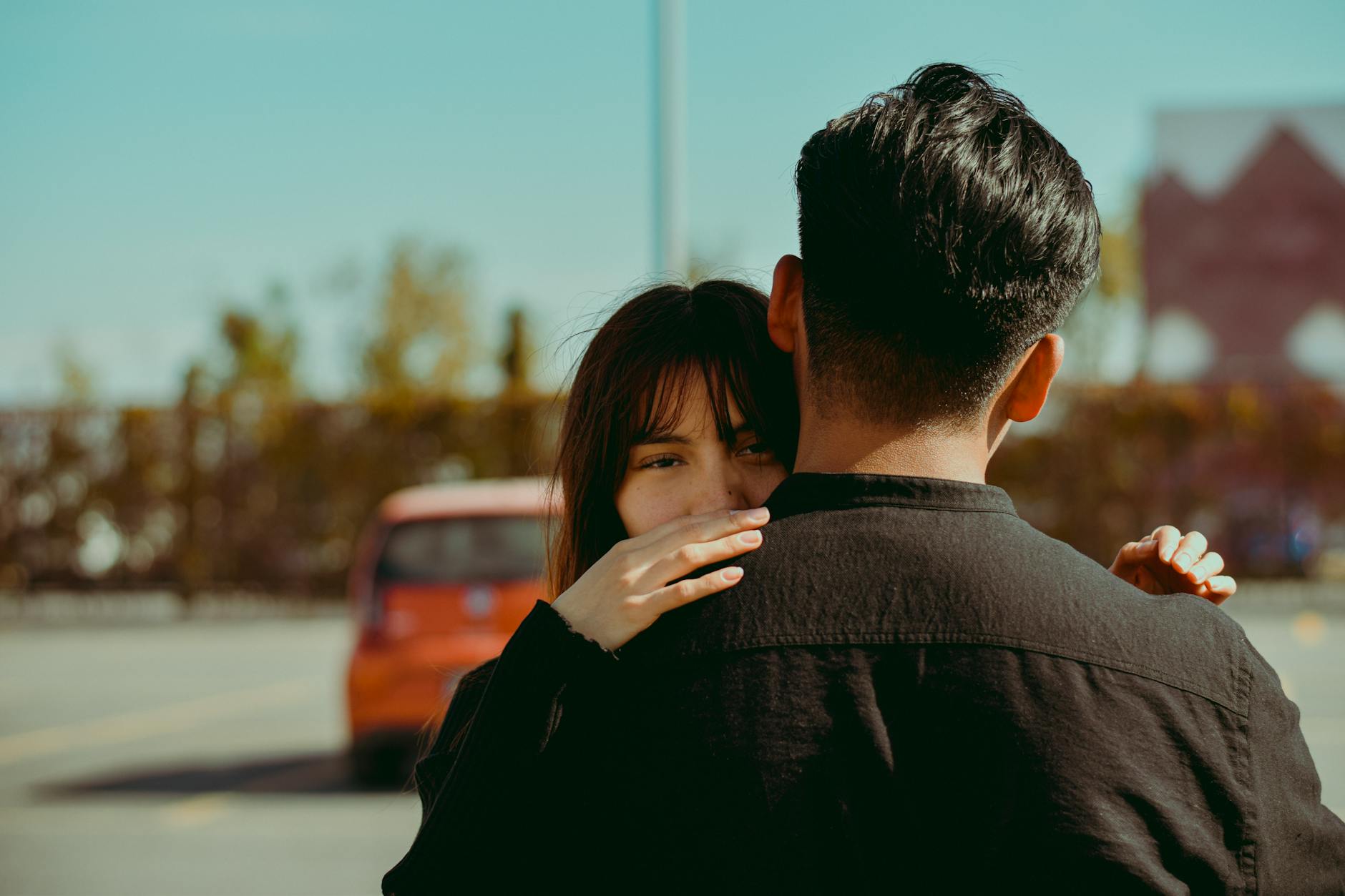 A couple sharing an intimate hug in an outdoor urban parking lot, under warm sunlight.