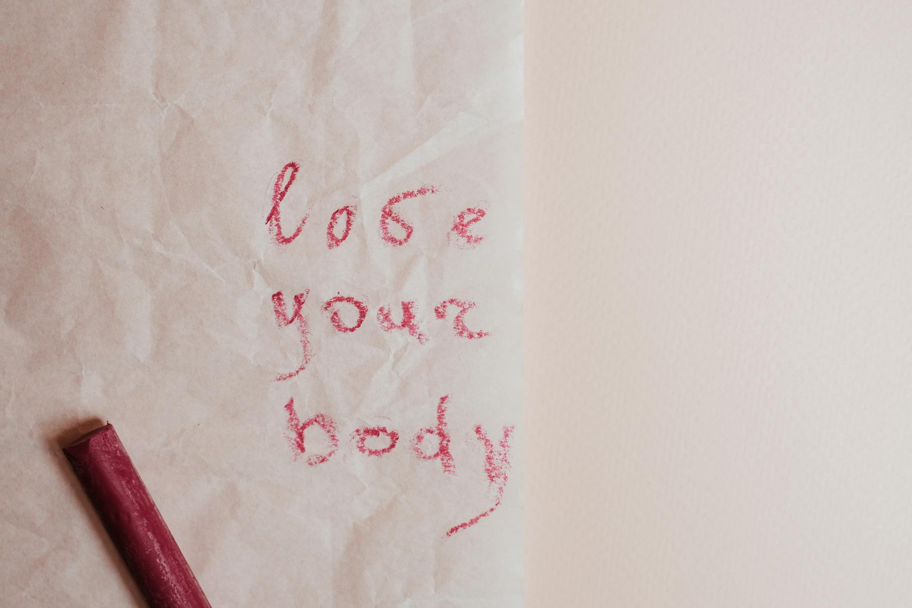 An inspiring 'love your body' message written on textured paper with red pastel crayon.