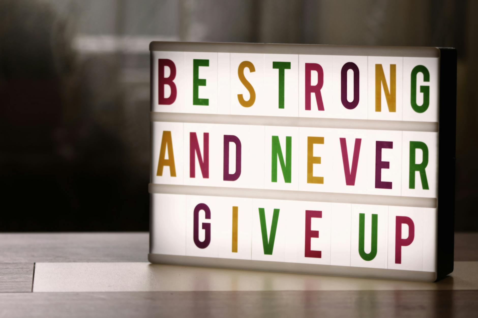 Inspirational lightbox displaying the motivational quote 'Be Strong and Never Give Up' indoors.
