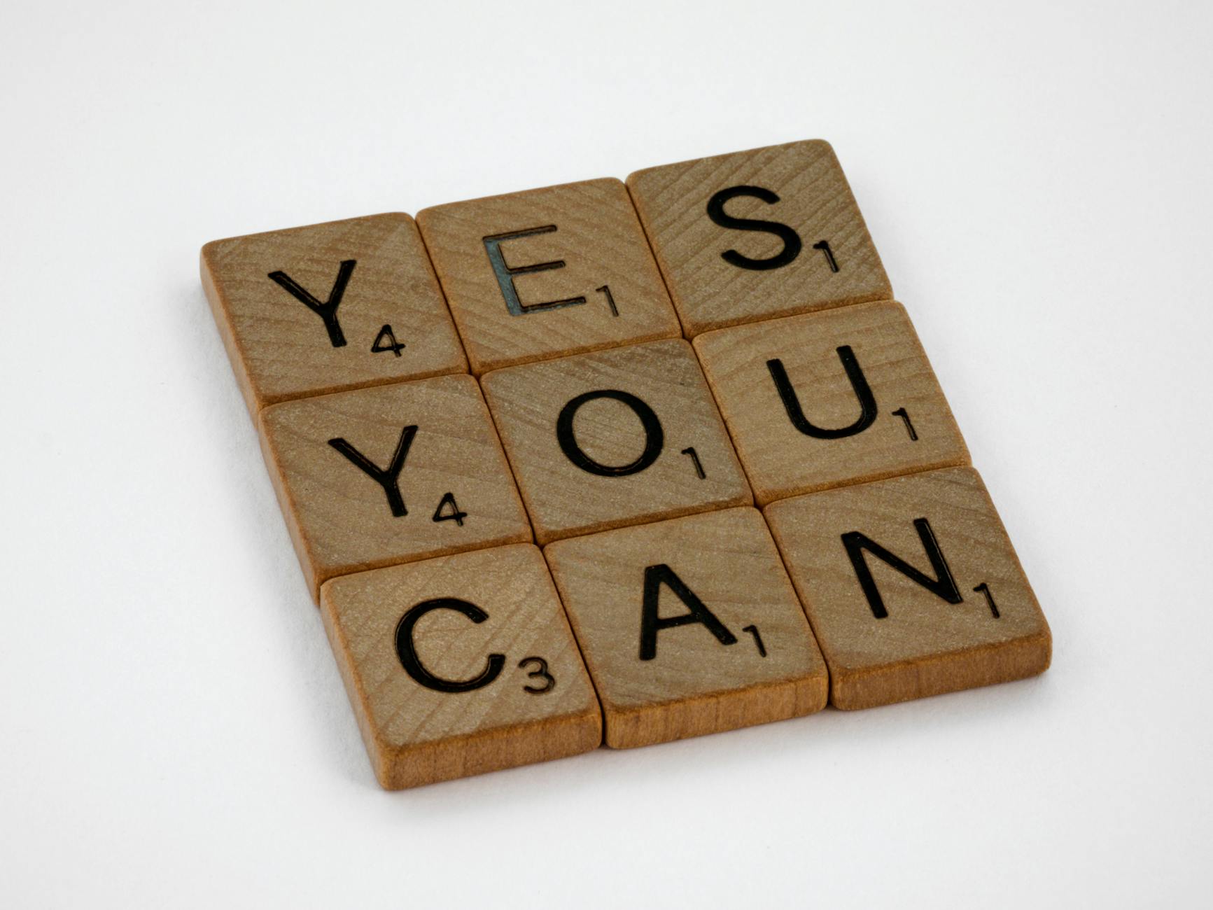 Wooden Scrabble tiles on white surface spelling 'Yes You Can,' promoting positivity and motivation.