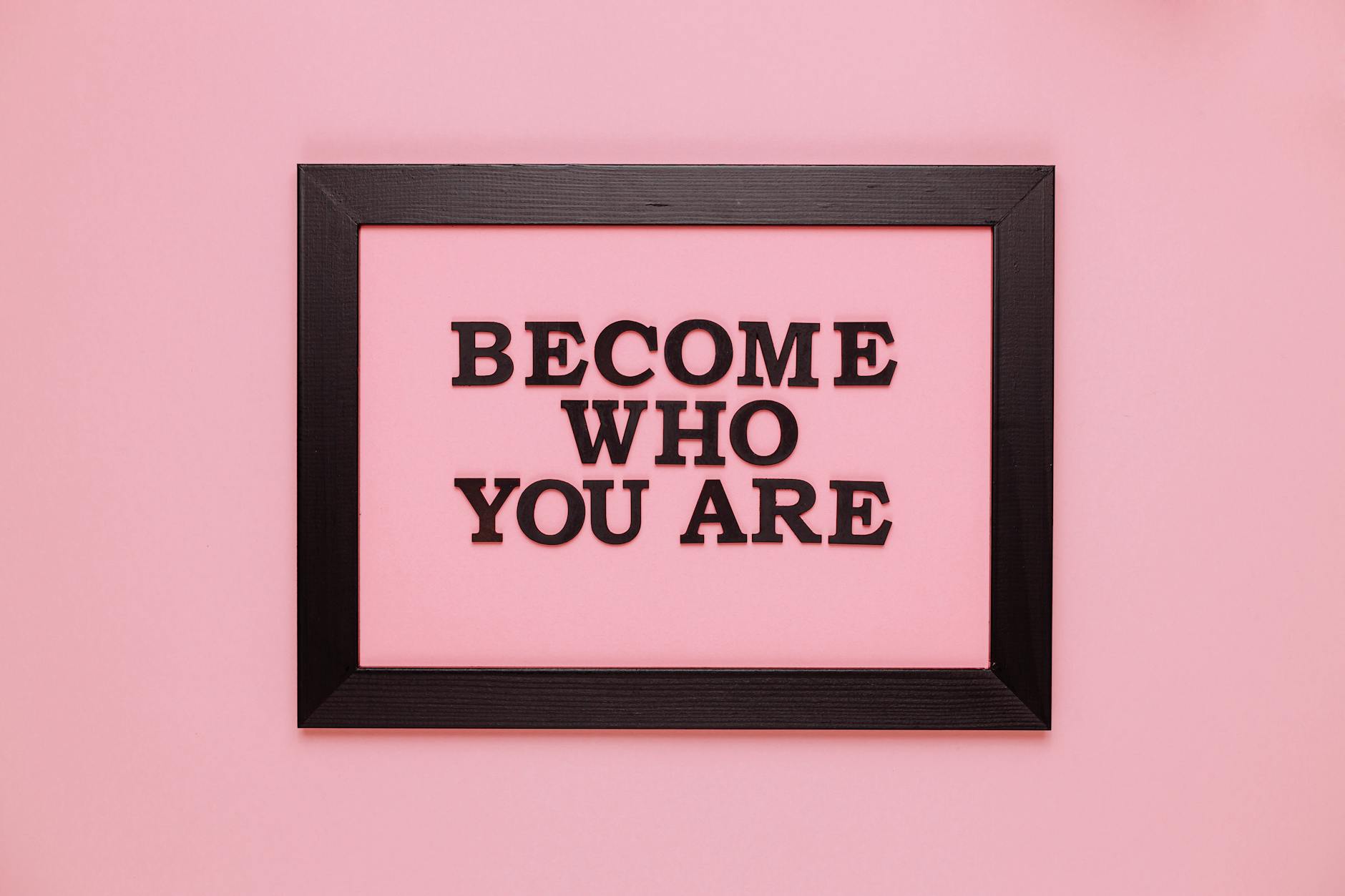 Inspiring quote 'Become Who You Are' framed on a vibrant pink wall, perfect for encouragement.