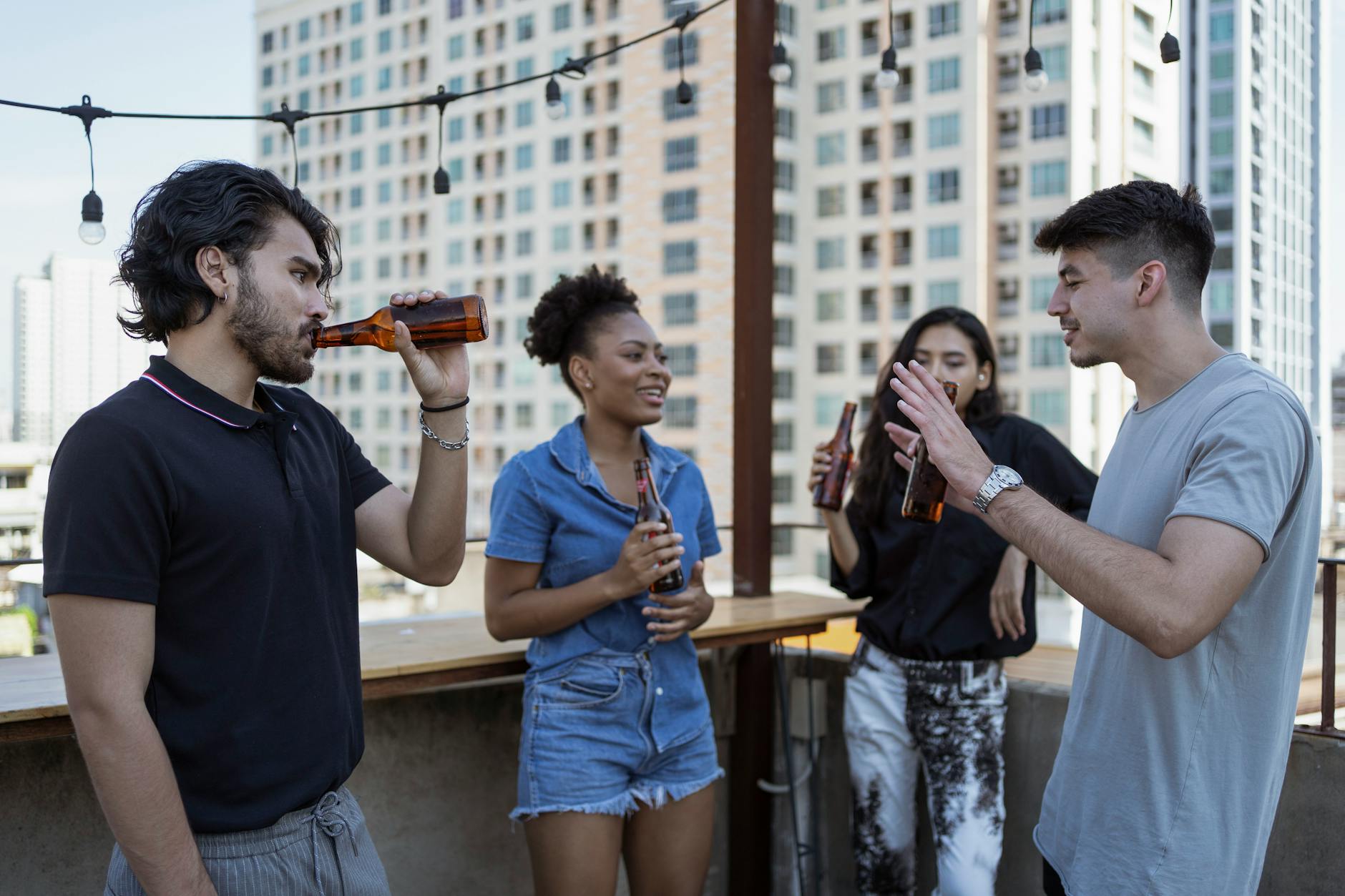 Group of friends enjoying drinks and conversation on a rooftop terrace with city skyline view.