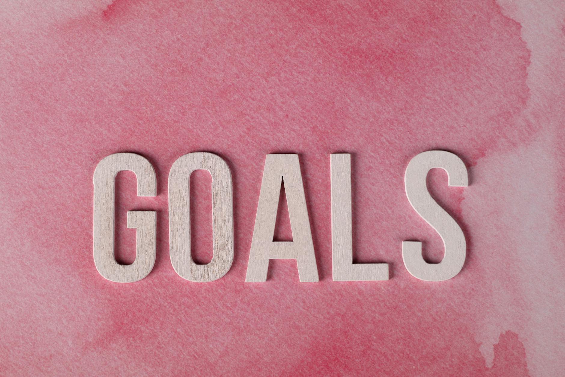 Motivational word 'GOALS' on a pink watercolor background for inspiration.