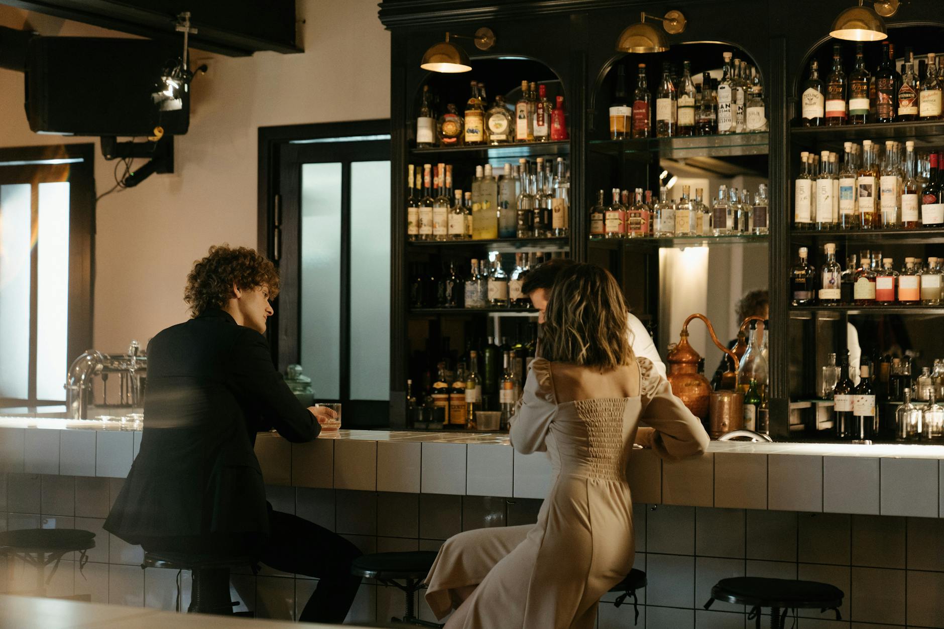 A man and woman engaging in lively conversation at an elegant bar, surrounded by bottles.