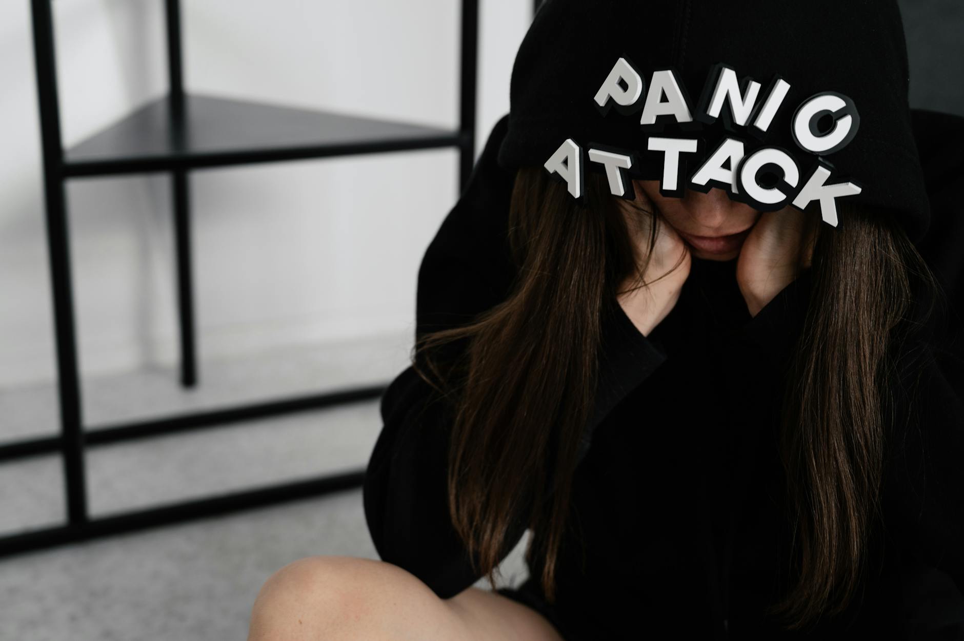 A woman sitting with 'PANIC ATTACK' on her hood, showing anxiety indoors.