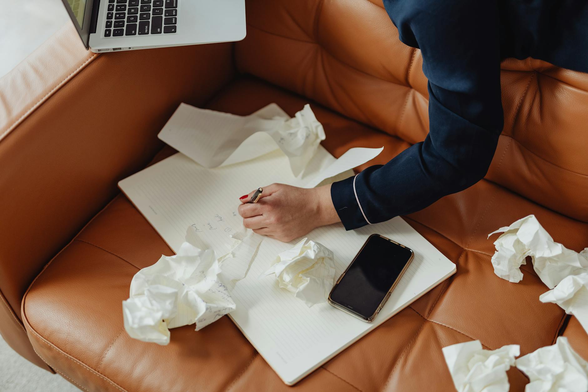 Person working on notebook with crumpled papers showing creative brainstorming.