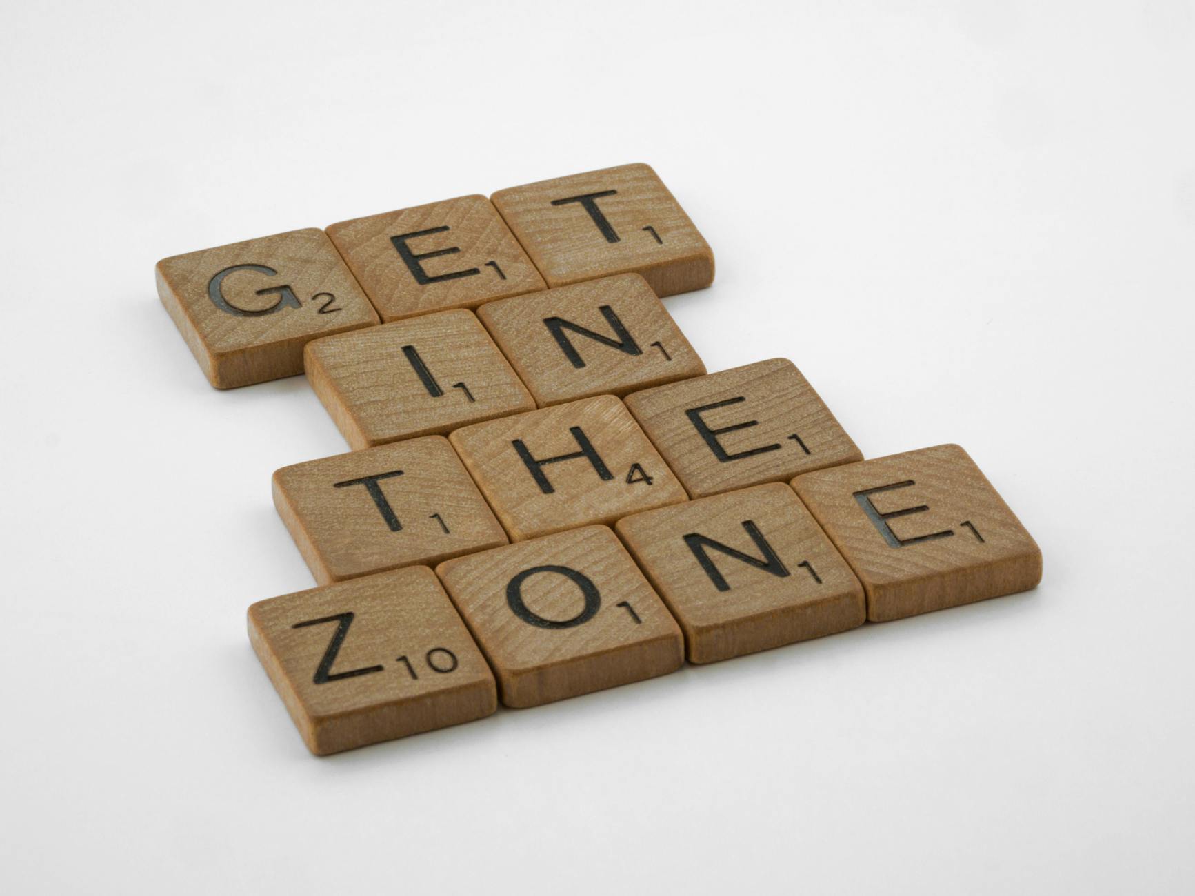 Wooden Scrabble tiles on white background spelling "Get in the Zone" for focus.