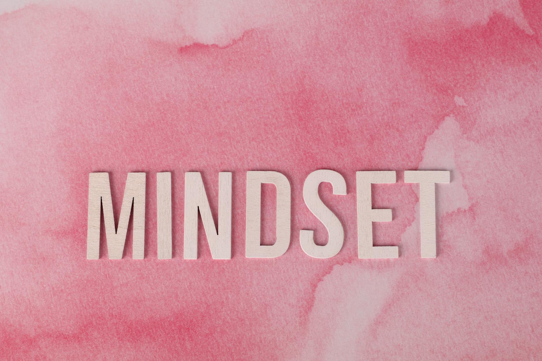 Wooden letters spelling 'MINDSET' on a textured pink background, symbolizing motivation.