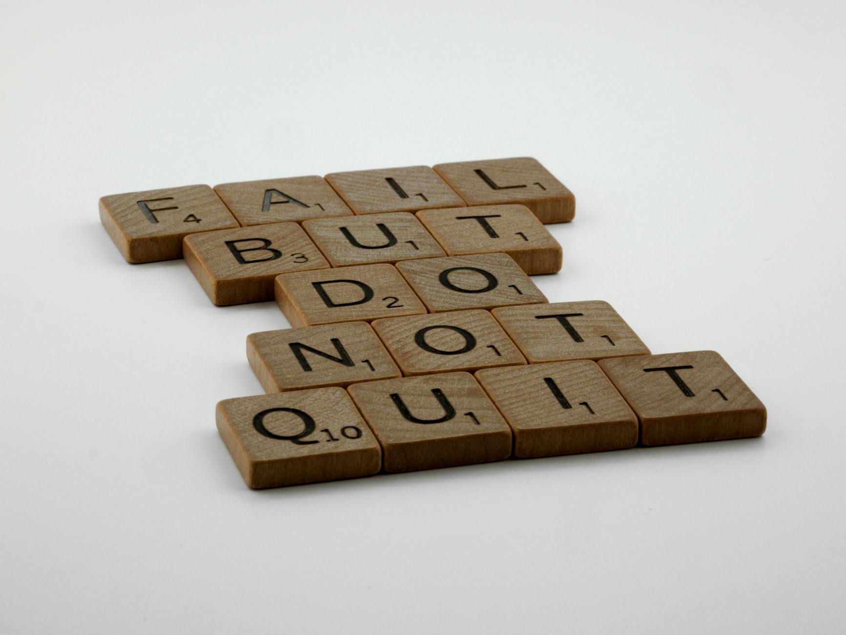 Wooden Scrabble tiles arranged to spell 'Fail but do not quit,' inspiring determination.