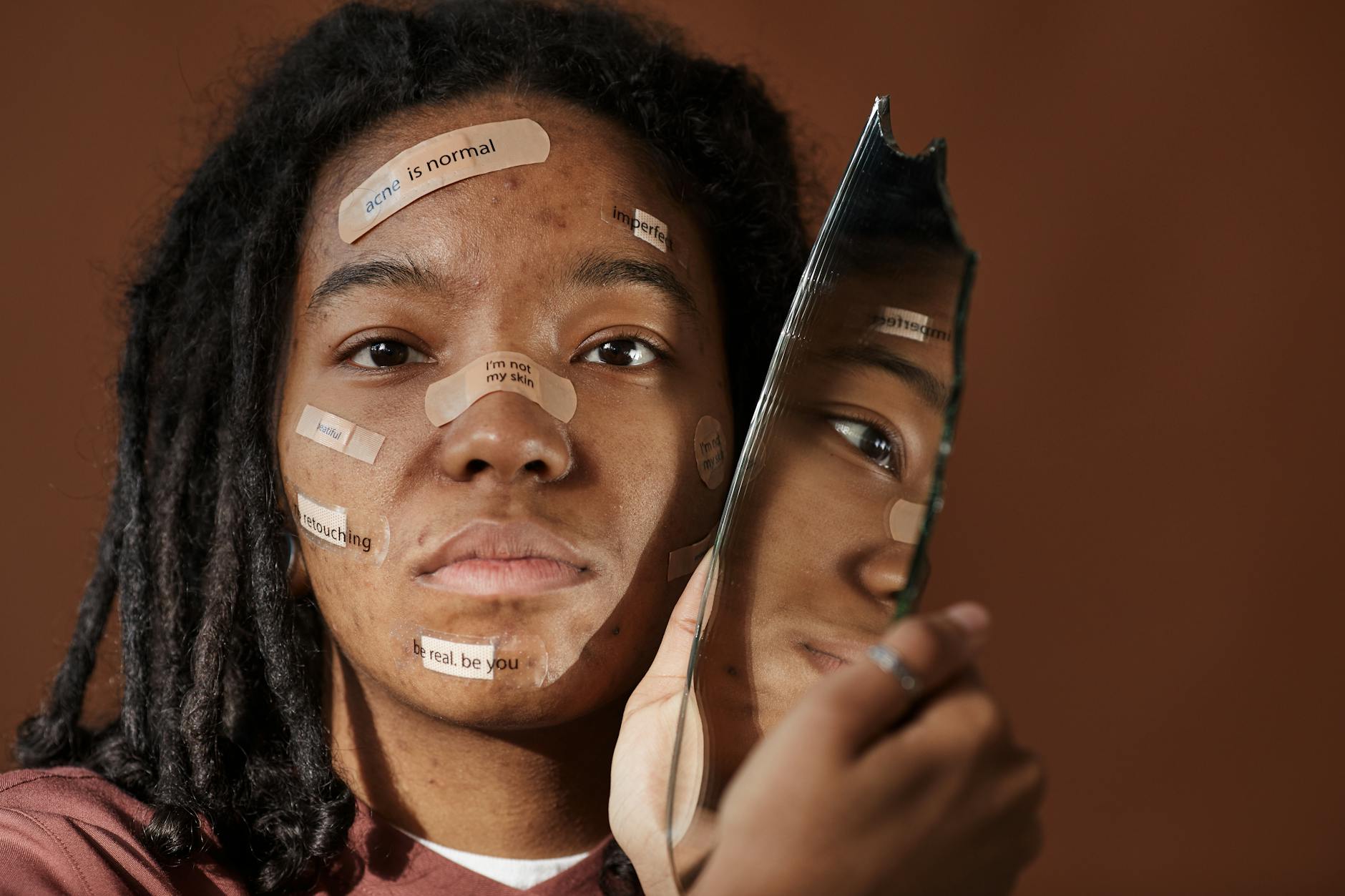 A powerful portrait of a woman embracing imperfections with positive messages on her face, holding a broken mirror.