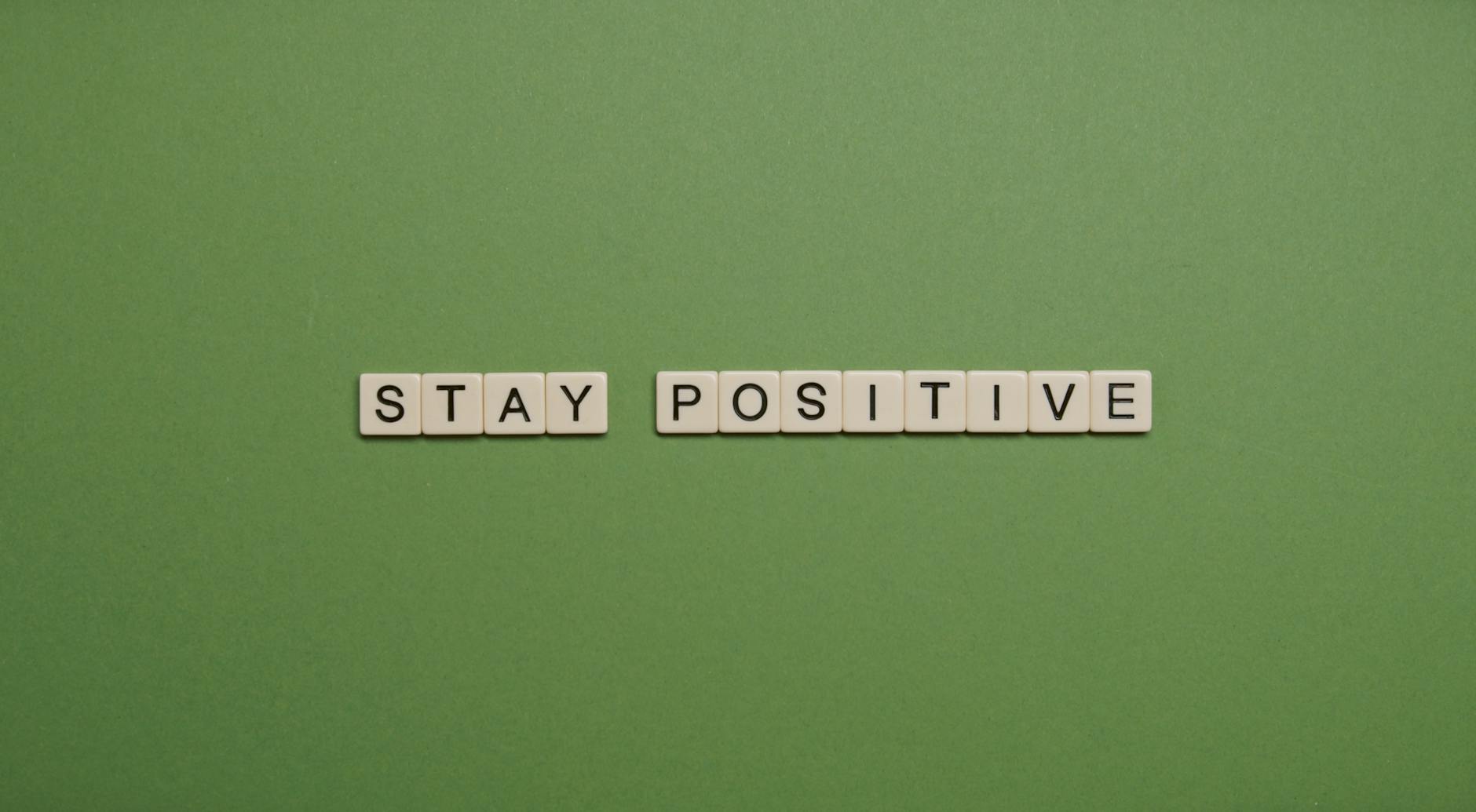 "Stay Positive" spelled with letter tiles on a green backdrop.