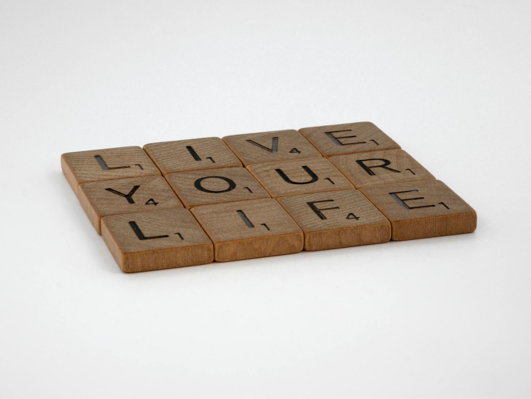 Wooden Scrabble tiles spell out 'Live Your Life' on a white surface. Encouraging and minimalist.