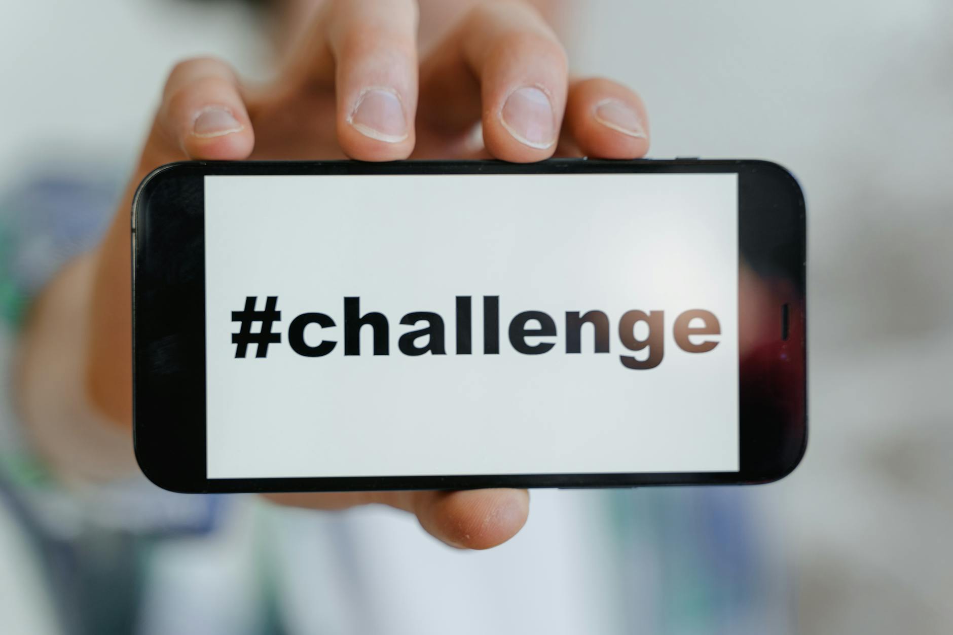 Close-up of a hand holding a smartphone displaying a '#challenge' hashtag.