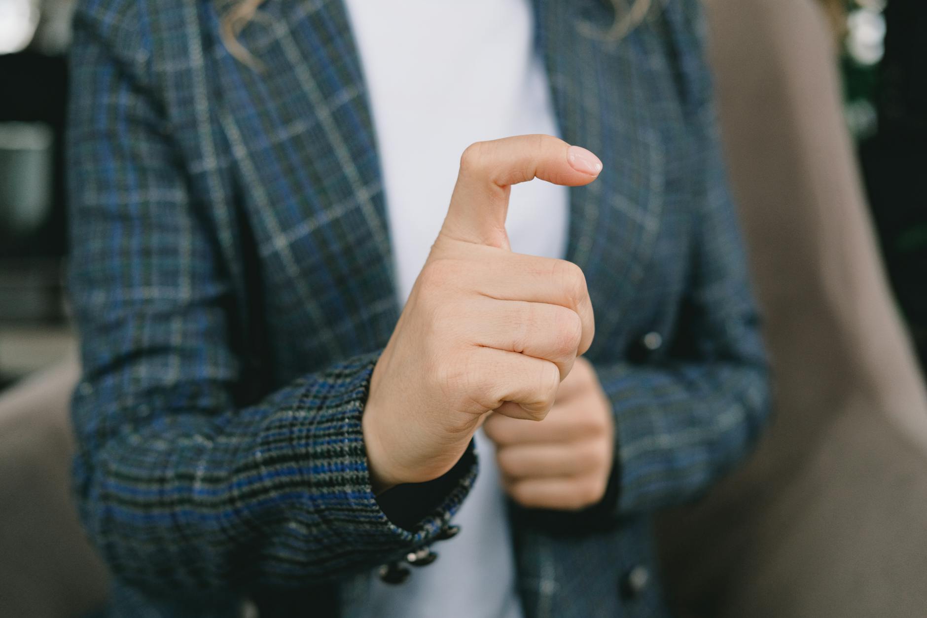 Crop anonymous female in smart casual clothes gesturing while sitting in comfortable armchair during sign language practice