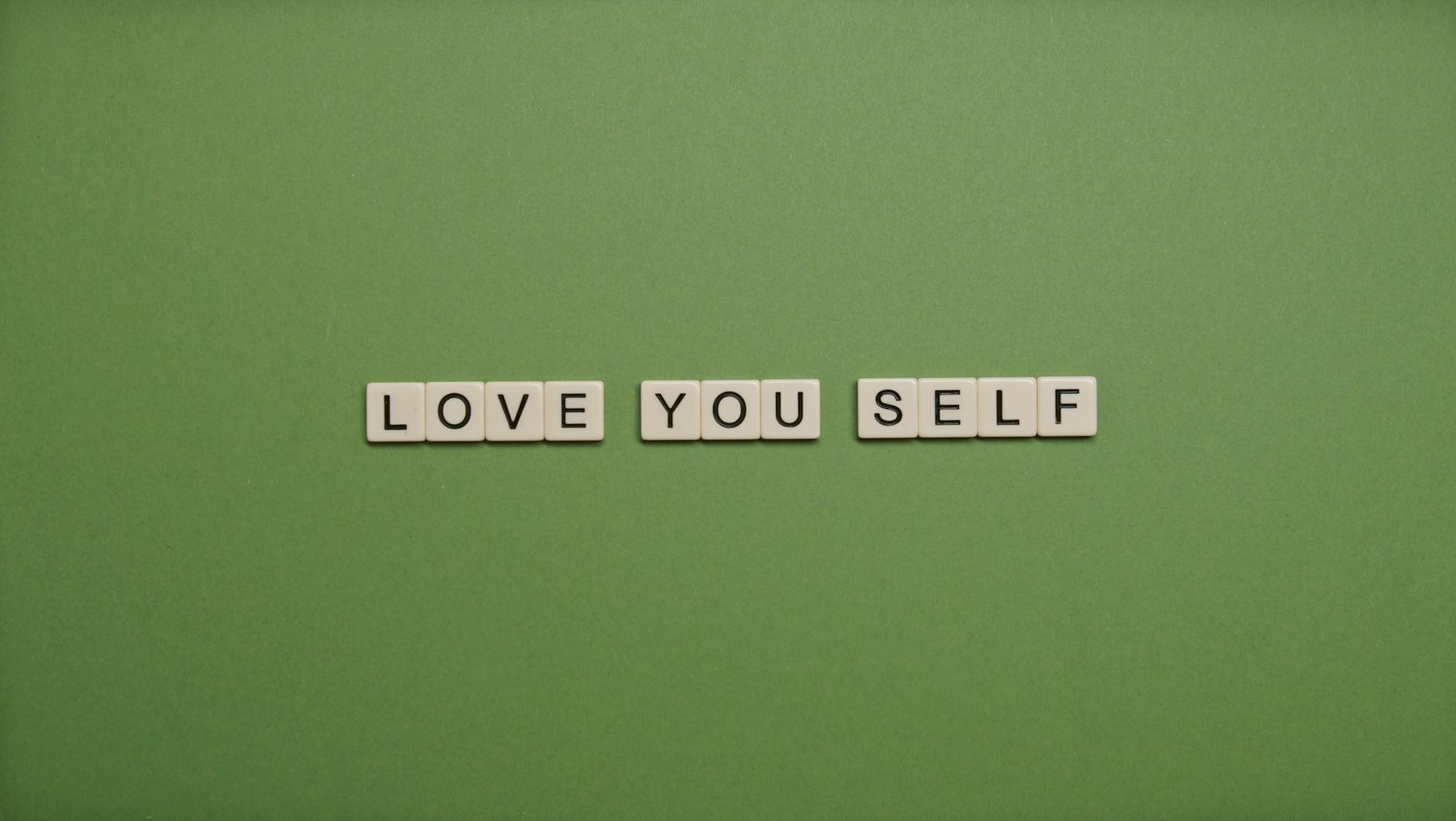 Positive message 'Love You Self' spelled with letter tiles on green background.