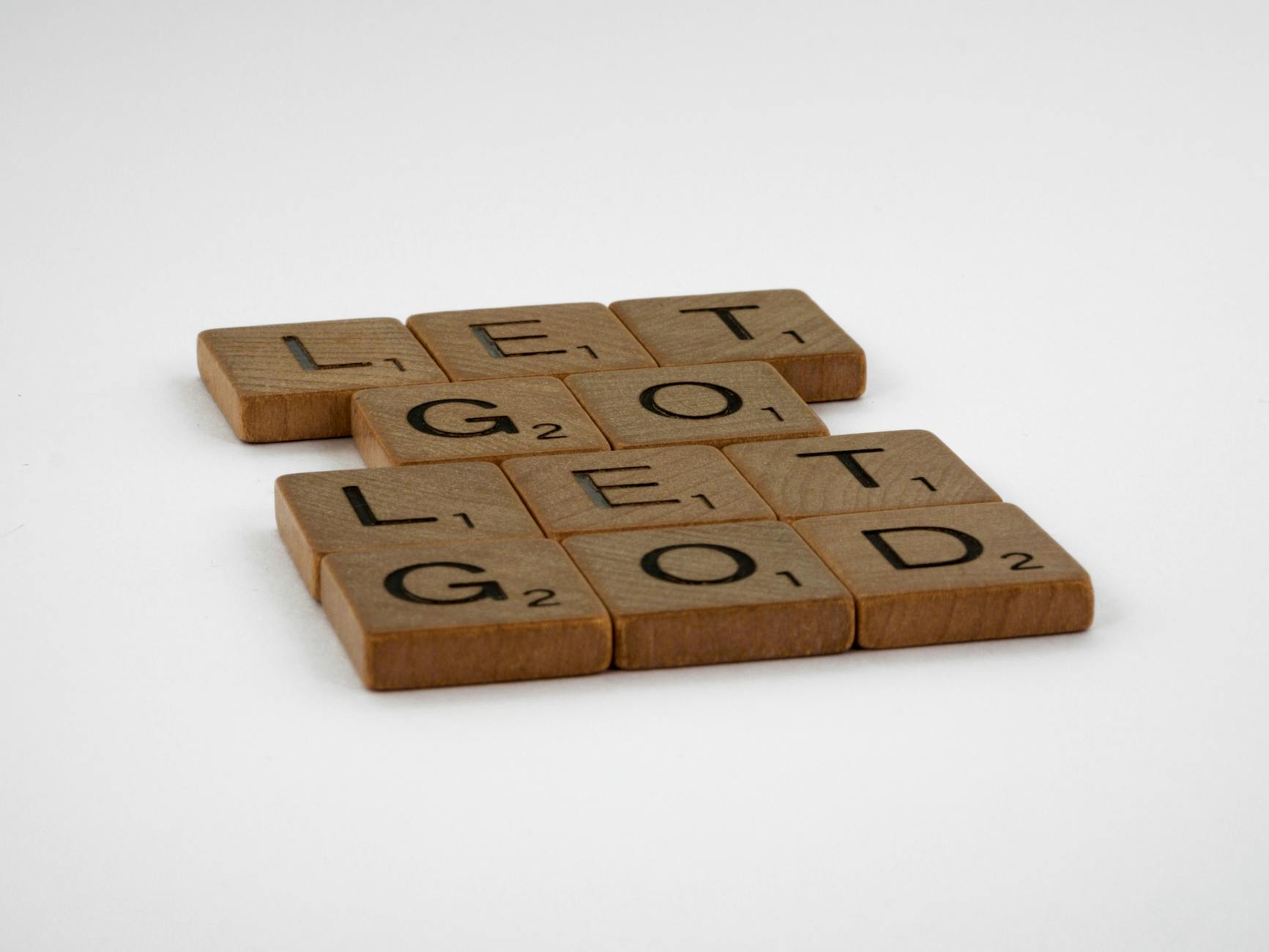 Scrabble tiles arranged to form the motivational phrase Let Go Let God on a white background.