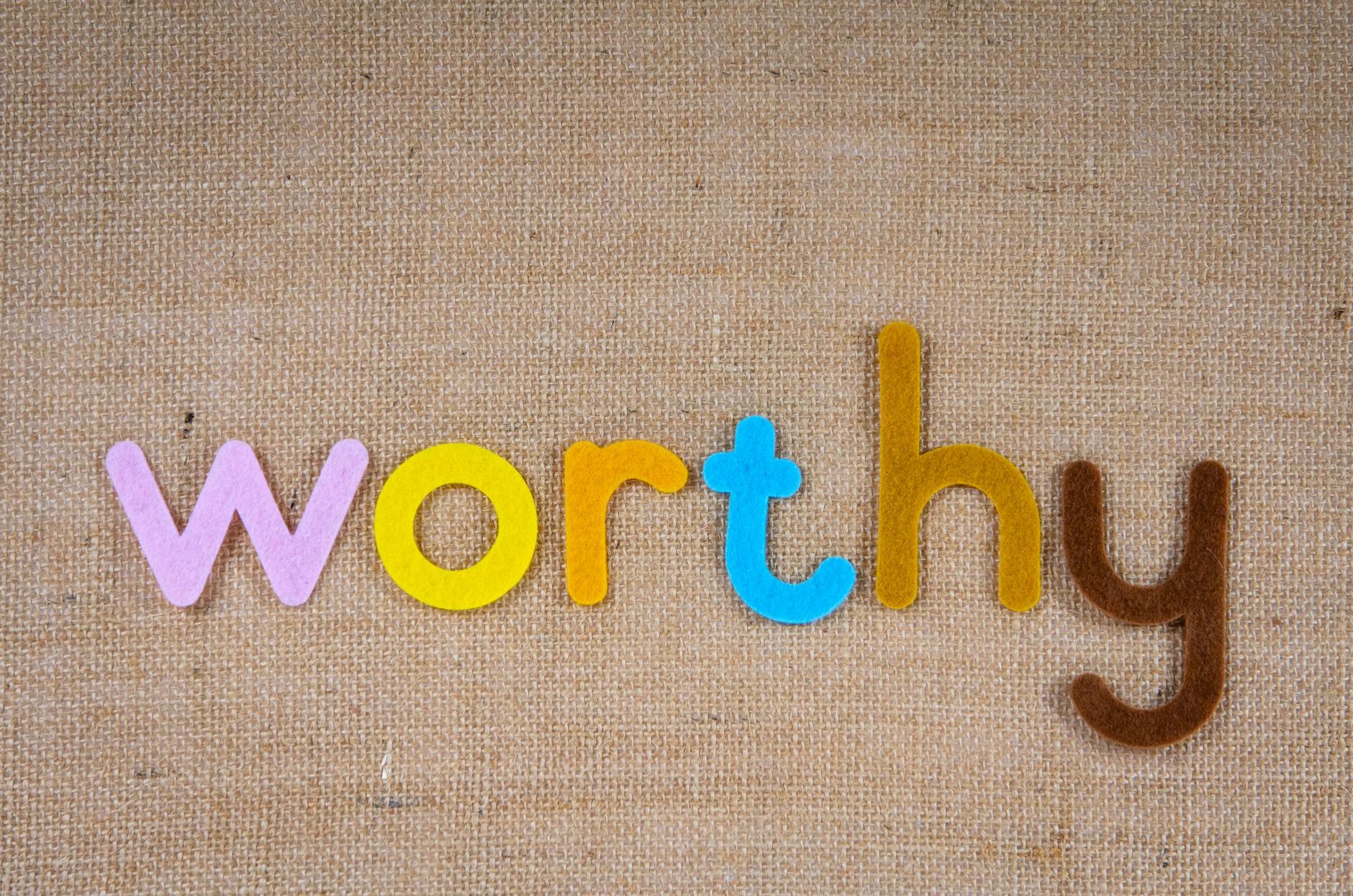 The word 'worthy' in colorful felt letters on a burlap texture, conveying positivity and value.