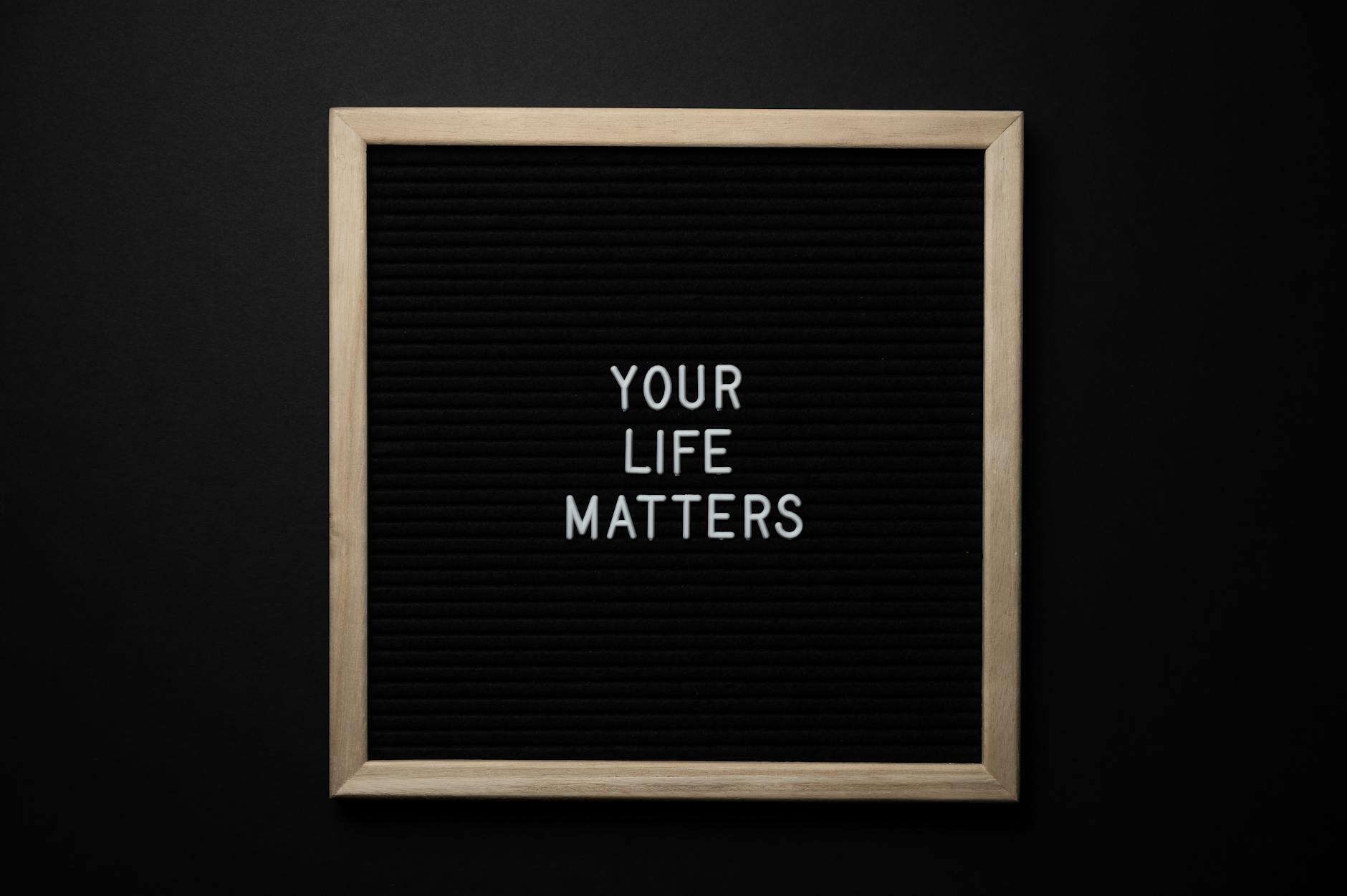 From above composition of black chalkboard with wooden frame with text YOUR LIFE MATTERS on center on black background