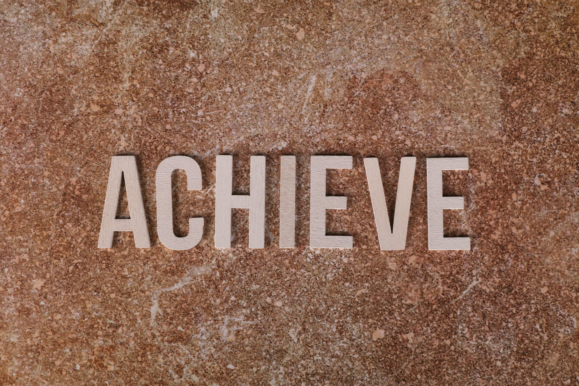 Wooden letters spelling 'ACHIEVE' on a textured brown surface, conveying motivation and success.