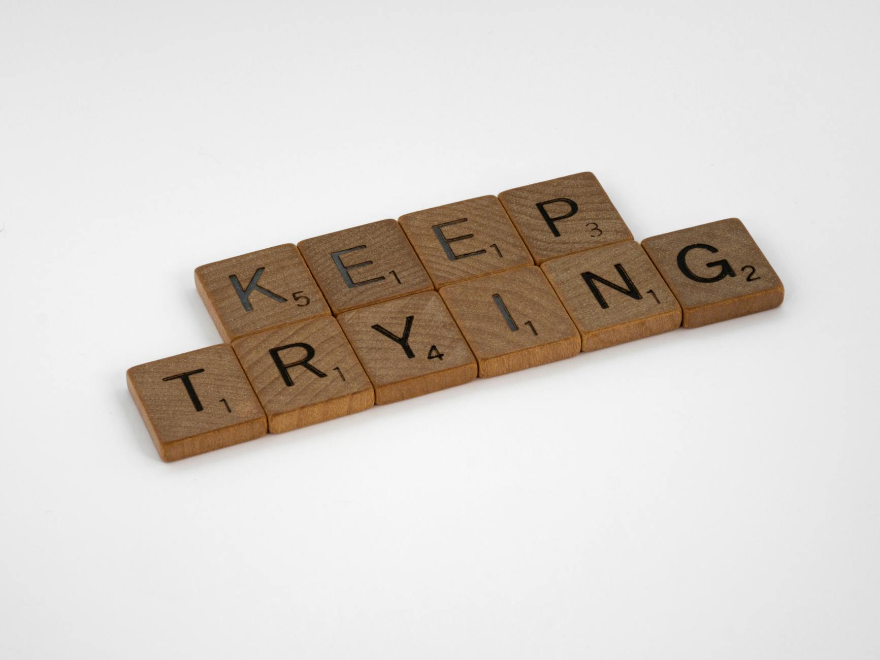 Scrabble tiles form an inspiring message 'Keep Trying' on a white background. Motivational and clean aesthetic.