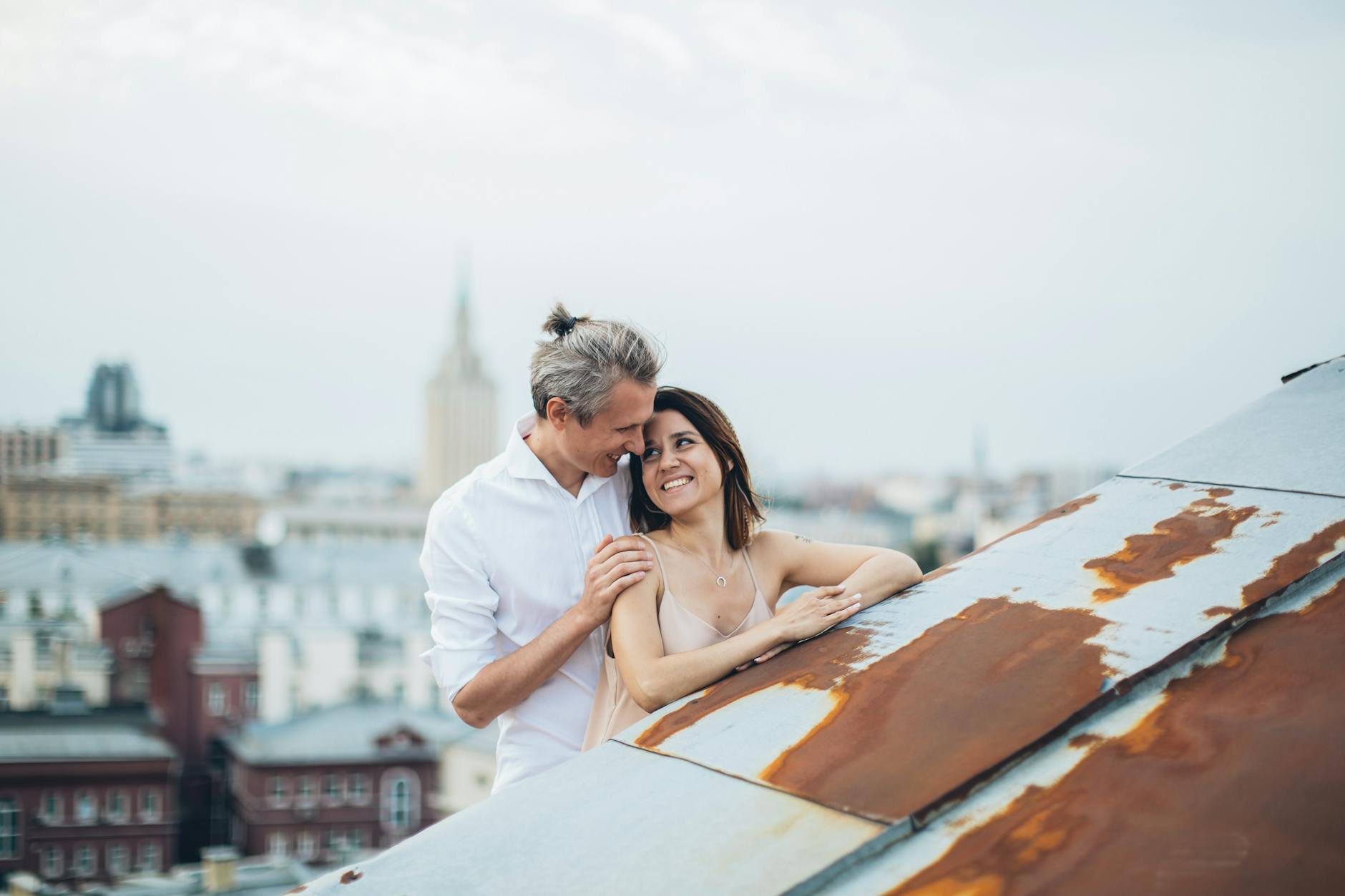Loving couple in casual clothes embracing on rooftop while smiling and looking at each other