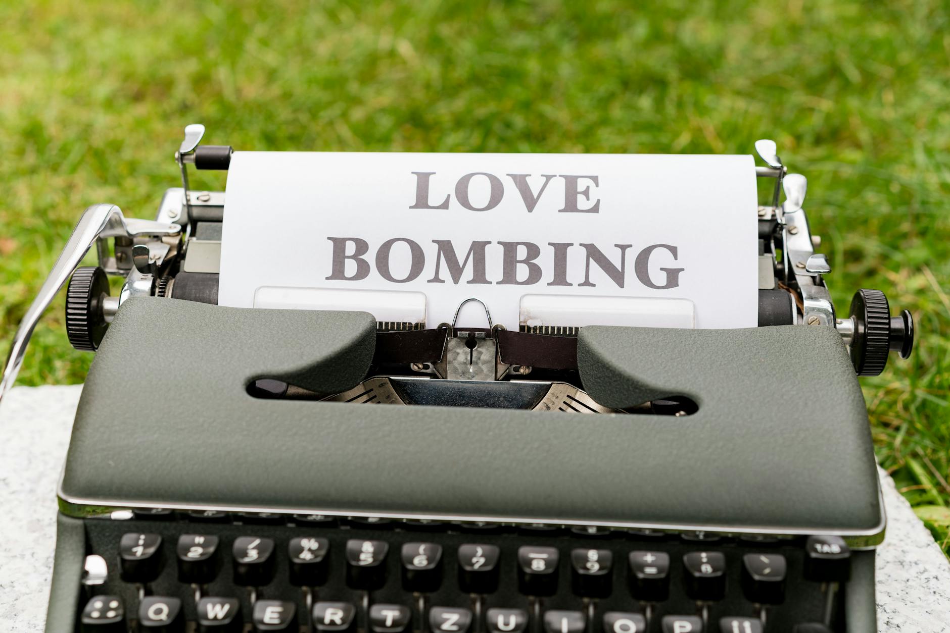 A vintage typewriter displaying the phrase 'Love Bombing' outdoors, symbolizing emotional manipulation.