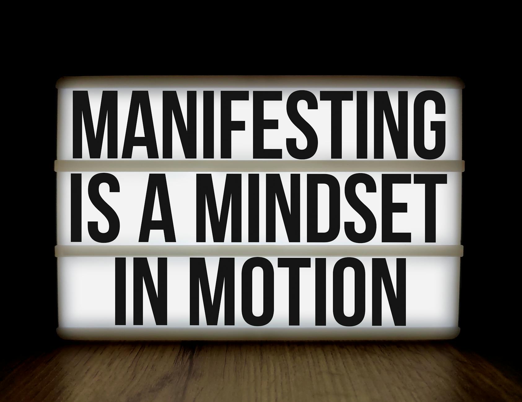 Inspirational quote 'Manifesting is a mindset in motion' on lightbox over dark background.