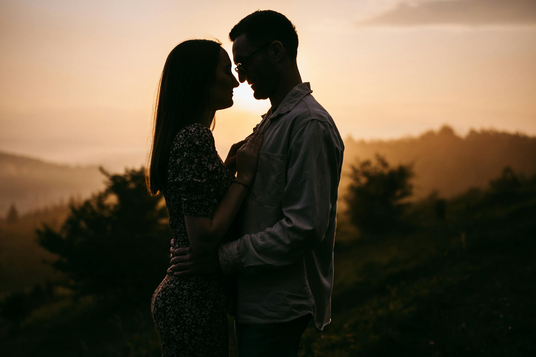 Silhouetted couple embracing romantically at sunrise in a mountainous landscape.