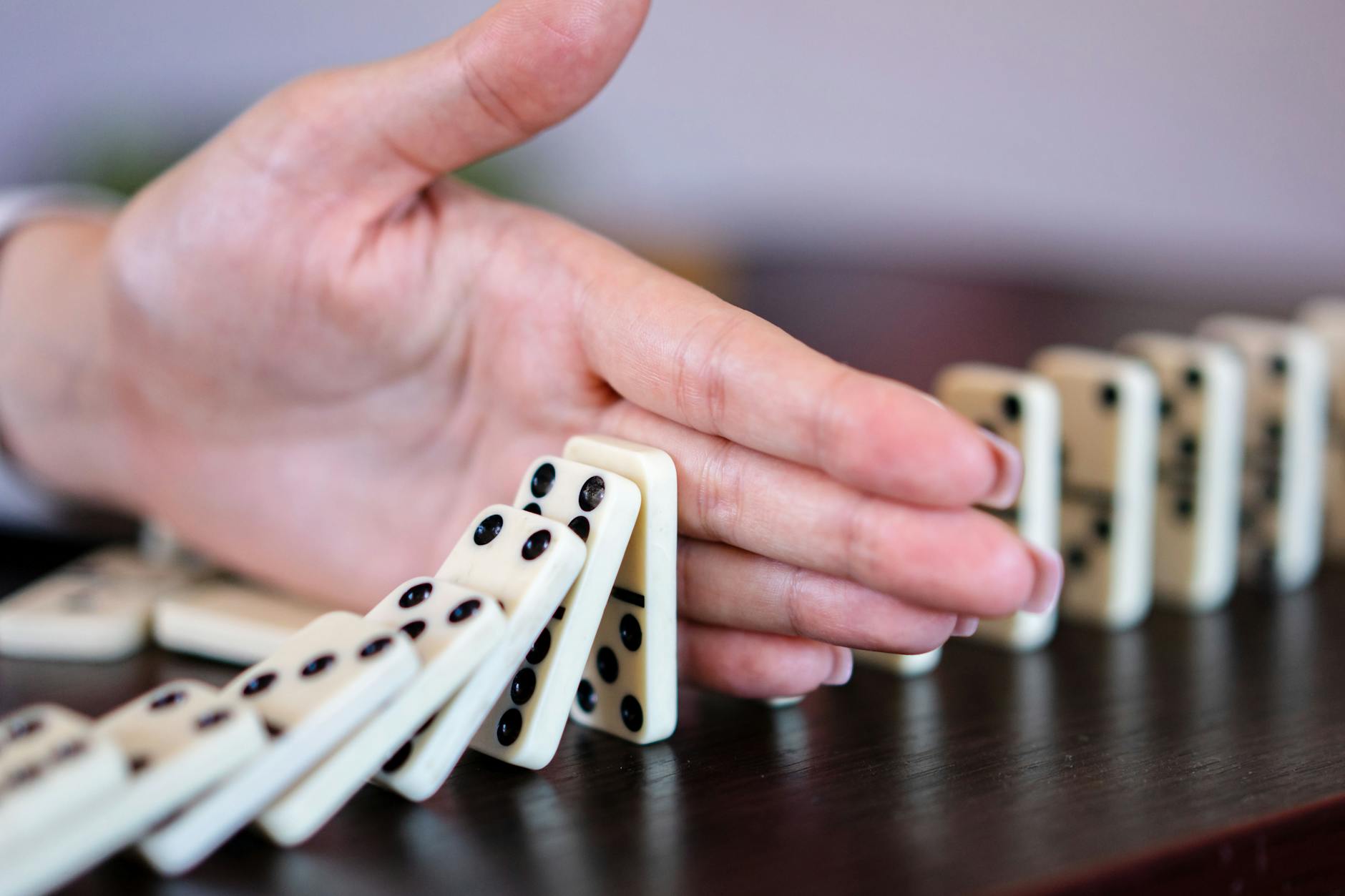 A close-up of a hand stopping a row of falling dominoes to illustrate strategy and control.