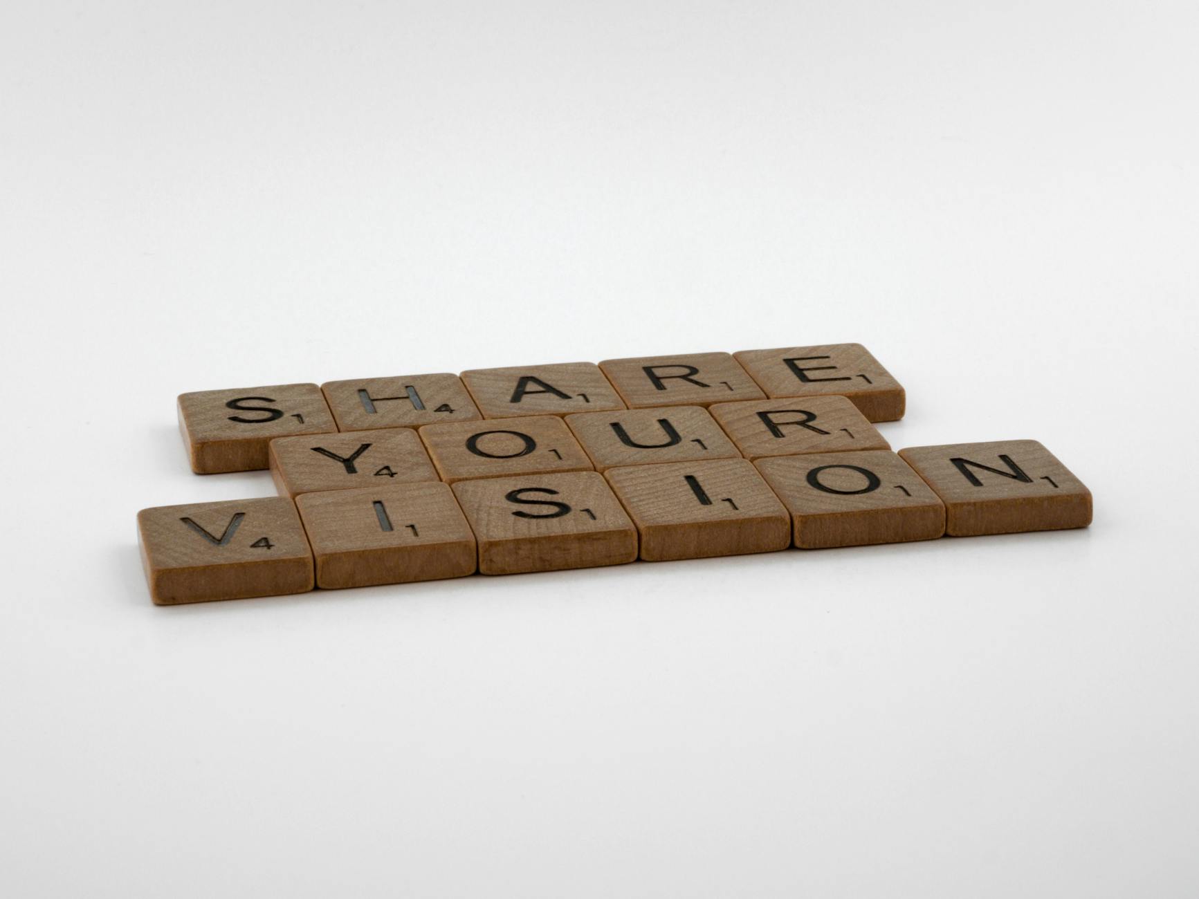 Wooden tiles spell 'Share Your Vision' on a white background, promoting creativity.